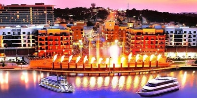 Branson Landing fountain show at night with colorful lights and riverboats