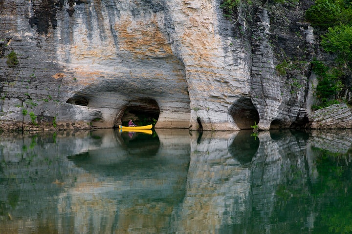 Yellow canoe paddling beneath dramatic limestone cave arches on the Buffalo National River